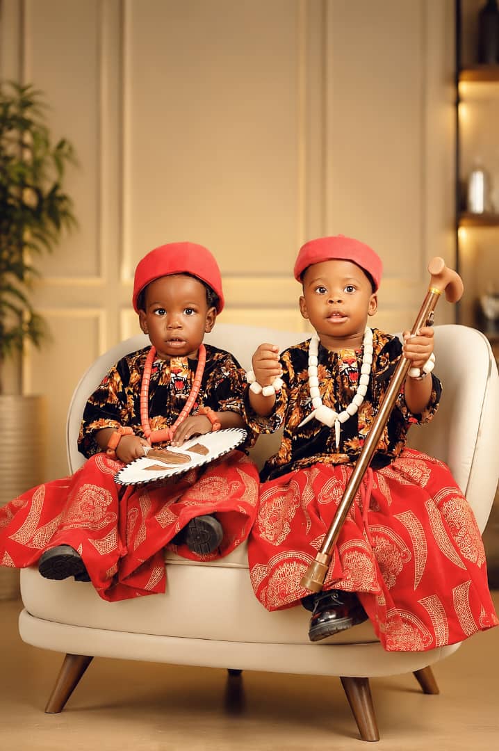 Twin toddlers in matching traditional red and black attire on a cream sofa