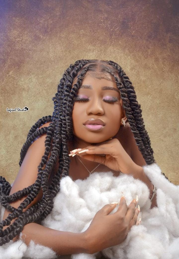 Woman with braided hair resting her chin on her hand against a warm backdrop