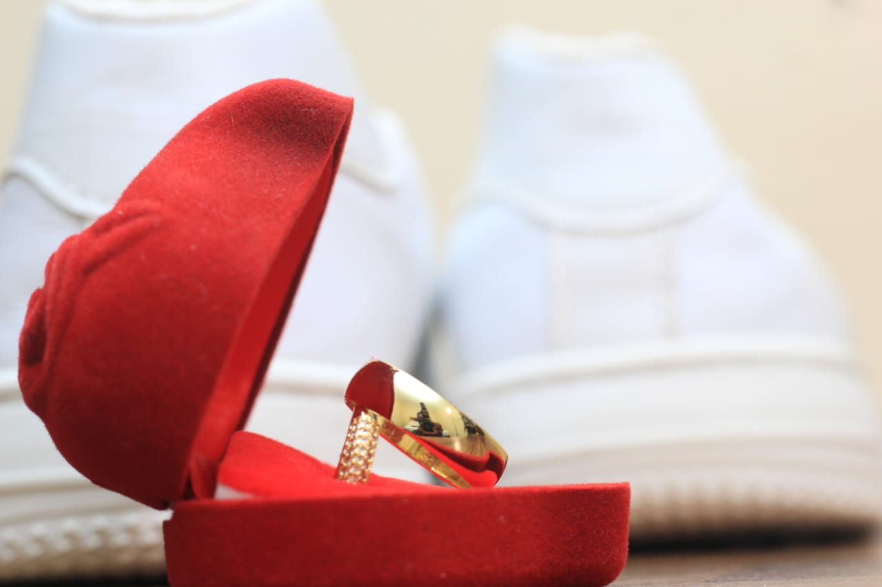 Wedding ring in an open red box beside white sneakers