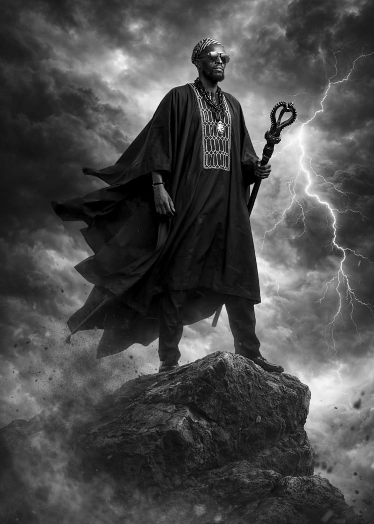 Dramatic black and white portrait of a man in flowing robes atop a rock beneath lightning