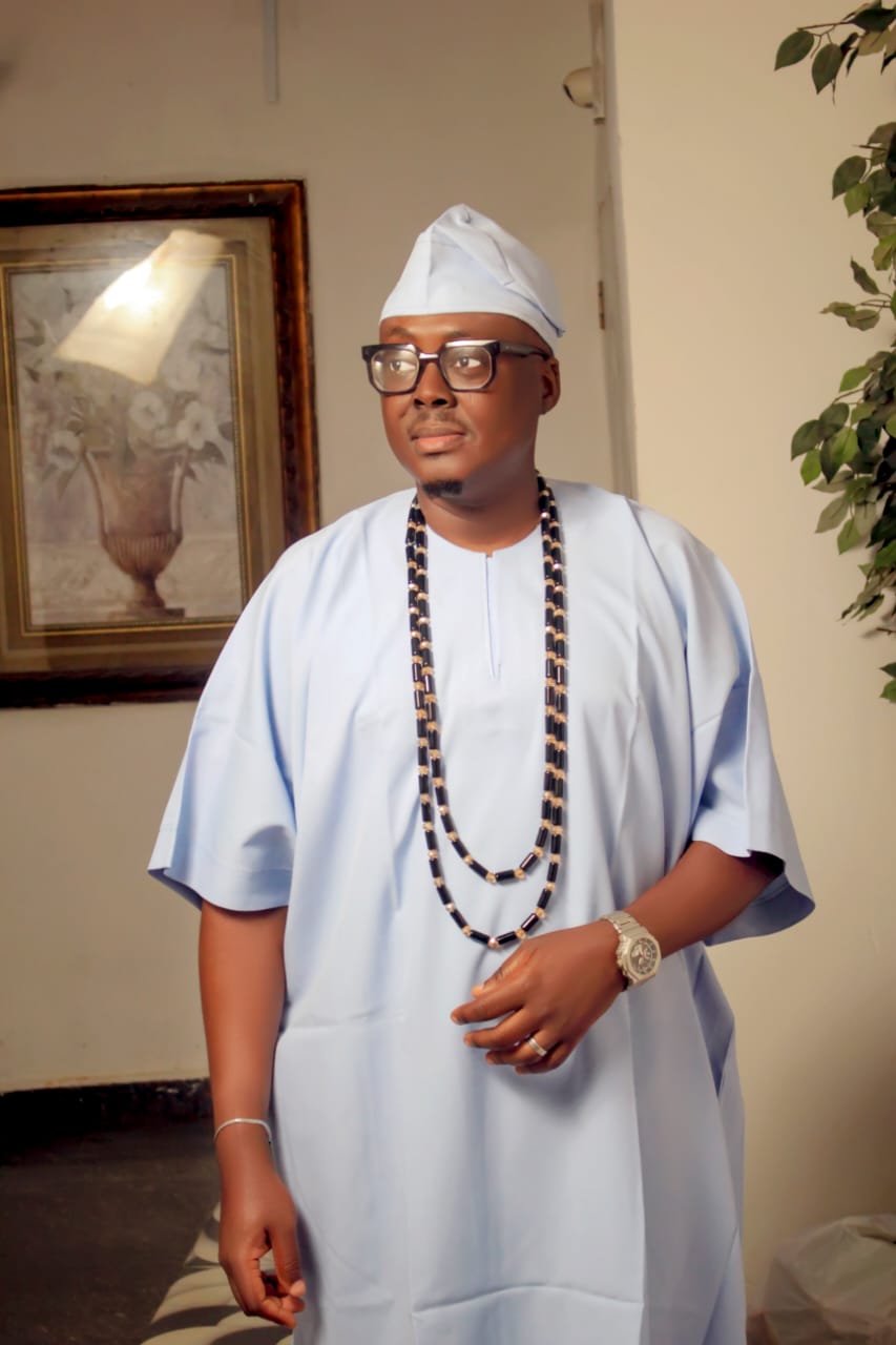Man in light blue traditional attire, glasses, and layered beads