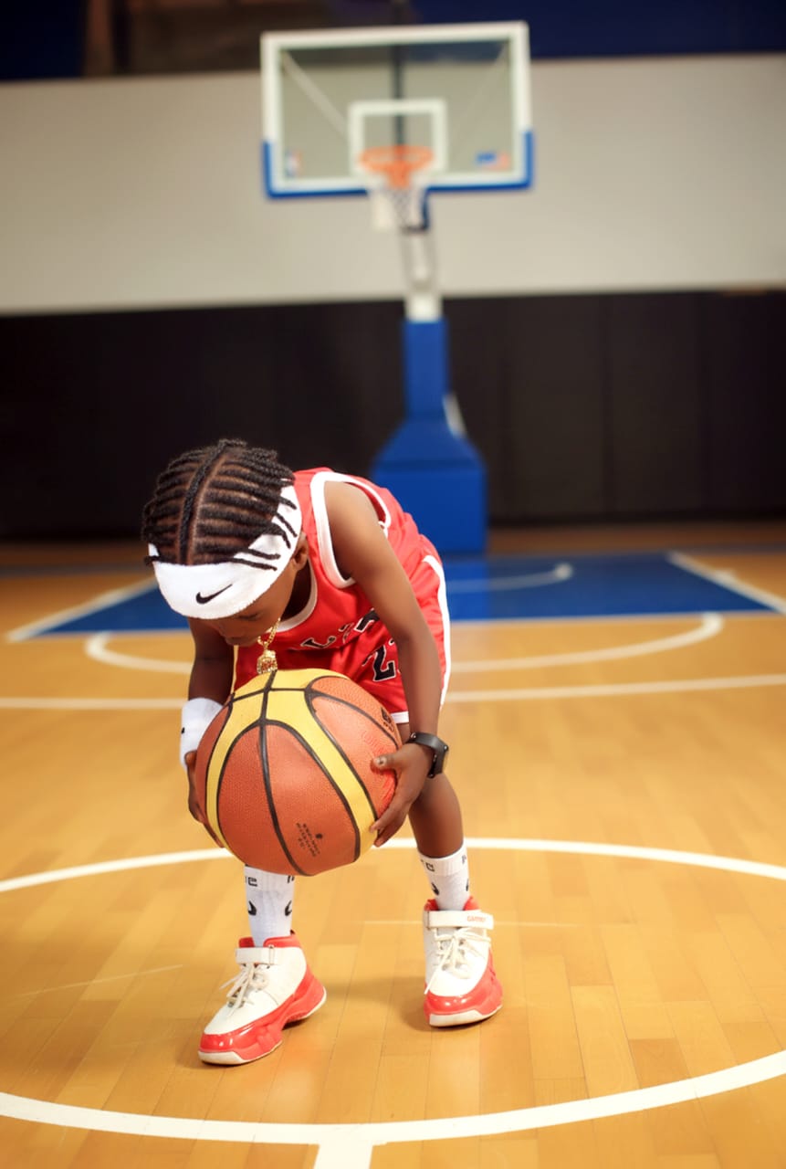 Young boy in a red basketball jersey dribbling on an indoor court