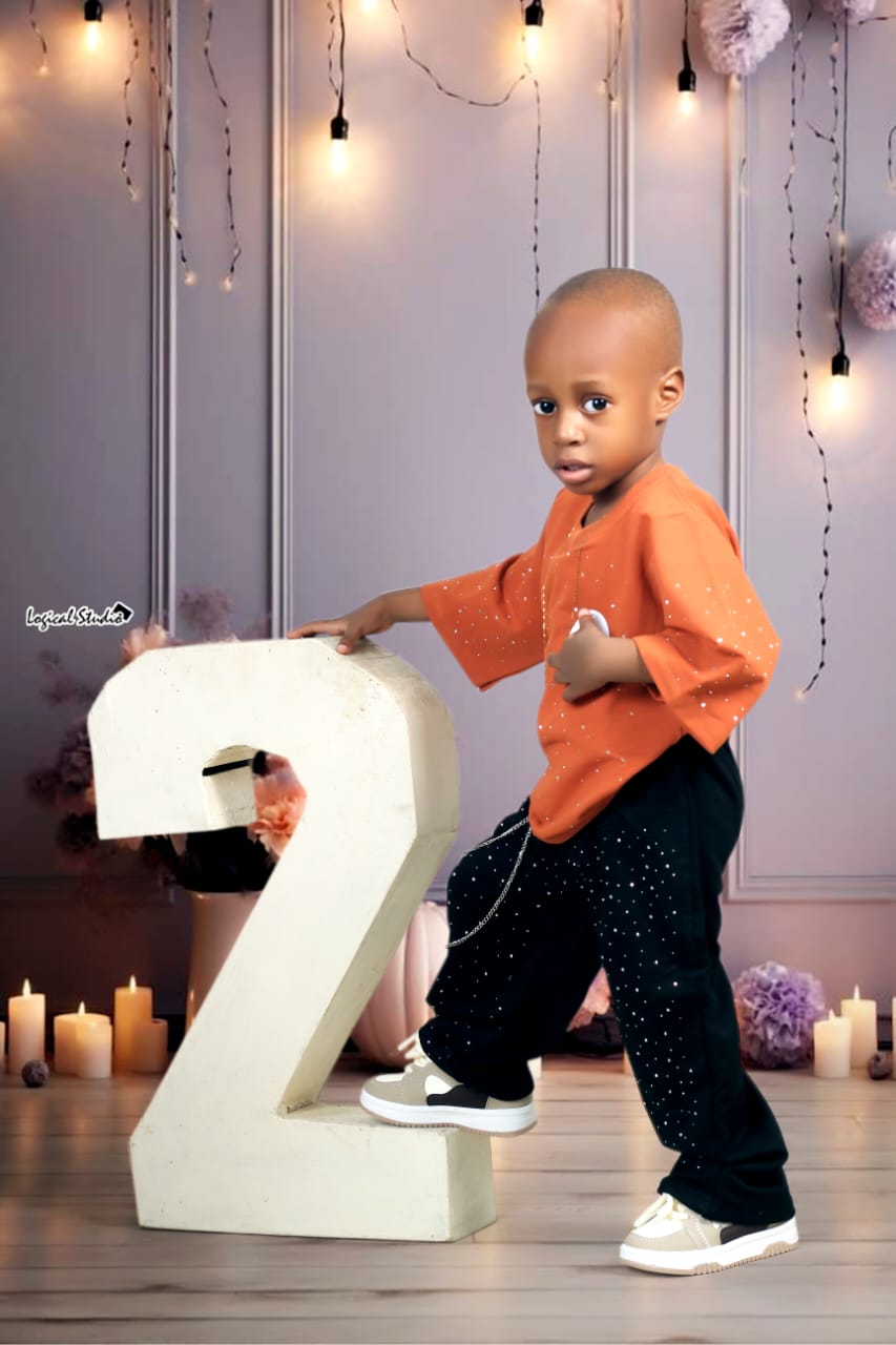 Toddler boy in an orange sparkle top posing beside a giant number two