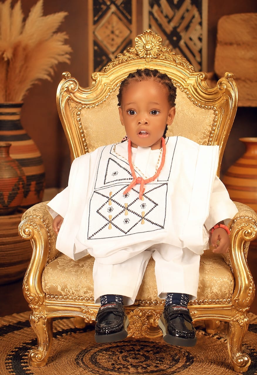 Toddler in white traditional attire seated on a gold throne chair