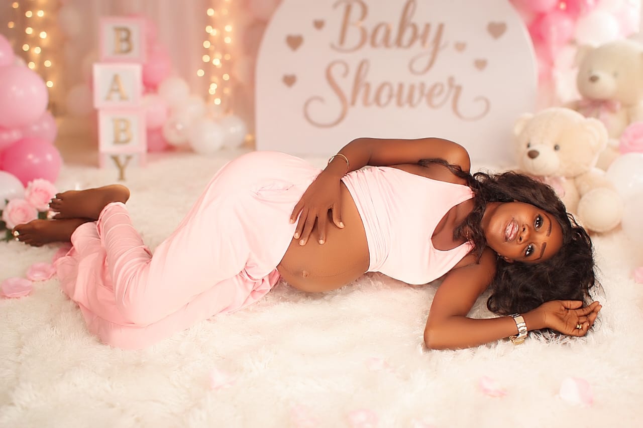 Pregnant woman reclining on a fur rug at a pink baby shower set