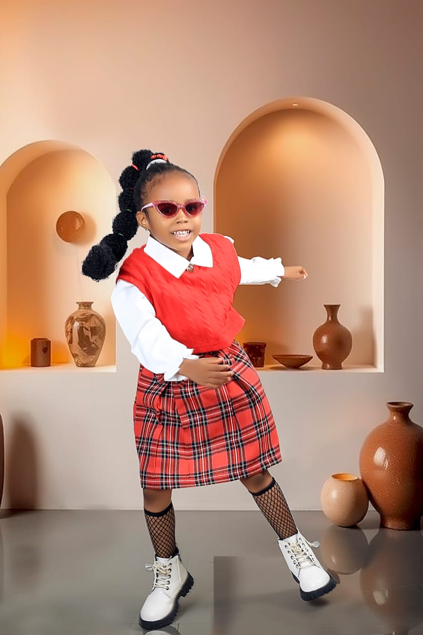 Girl in a red plaid skirt and sunglasses striking a playful dance pose