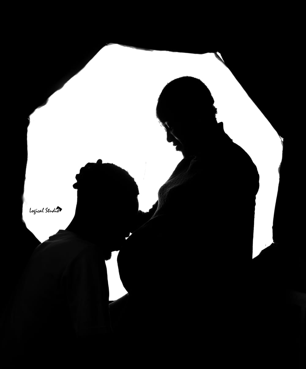 Silhouette of a couple embracing a pregnant belly against a bright backlit backdrop