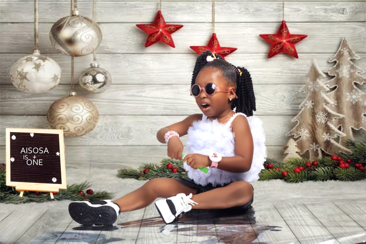 Toddler girl in white feathered outfit and sunglasses at a Christmas-themed first birthday shoot