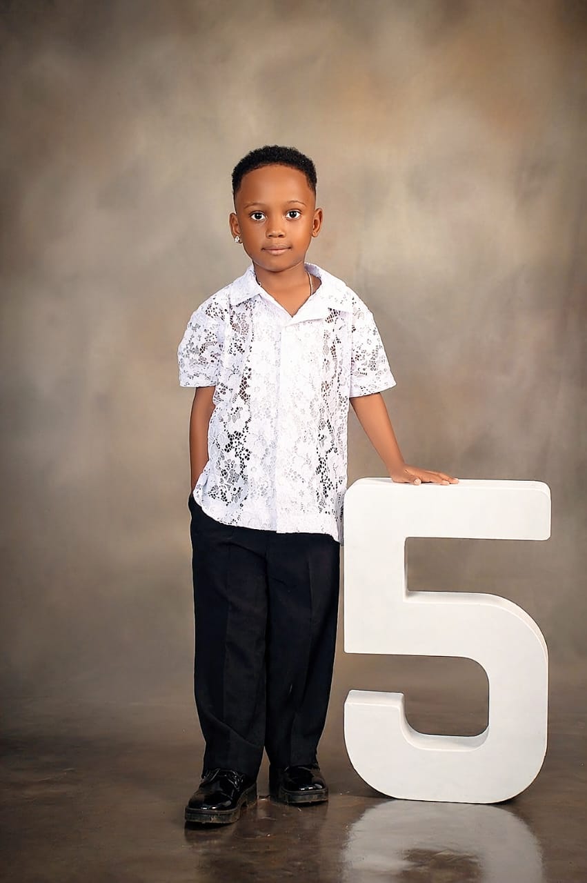 Boy in a white lace shirt standing beside a giant number five