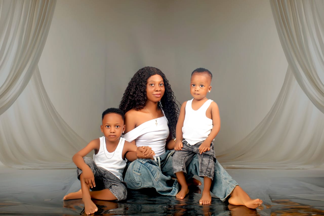 Mother seated with her two sons in matching denim and white outfits against a draped backdrop