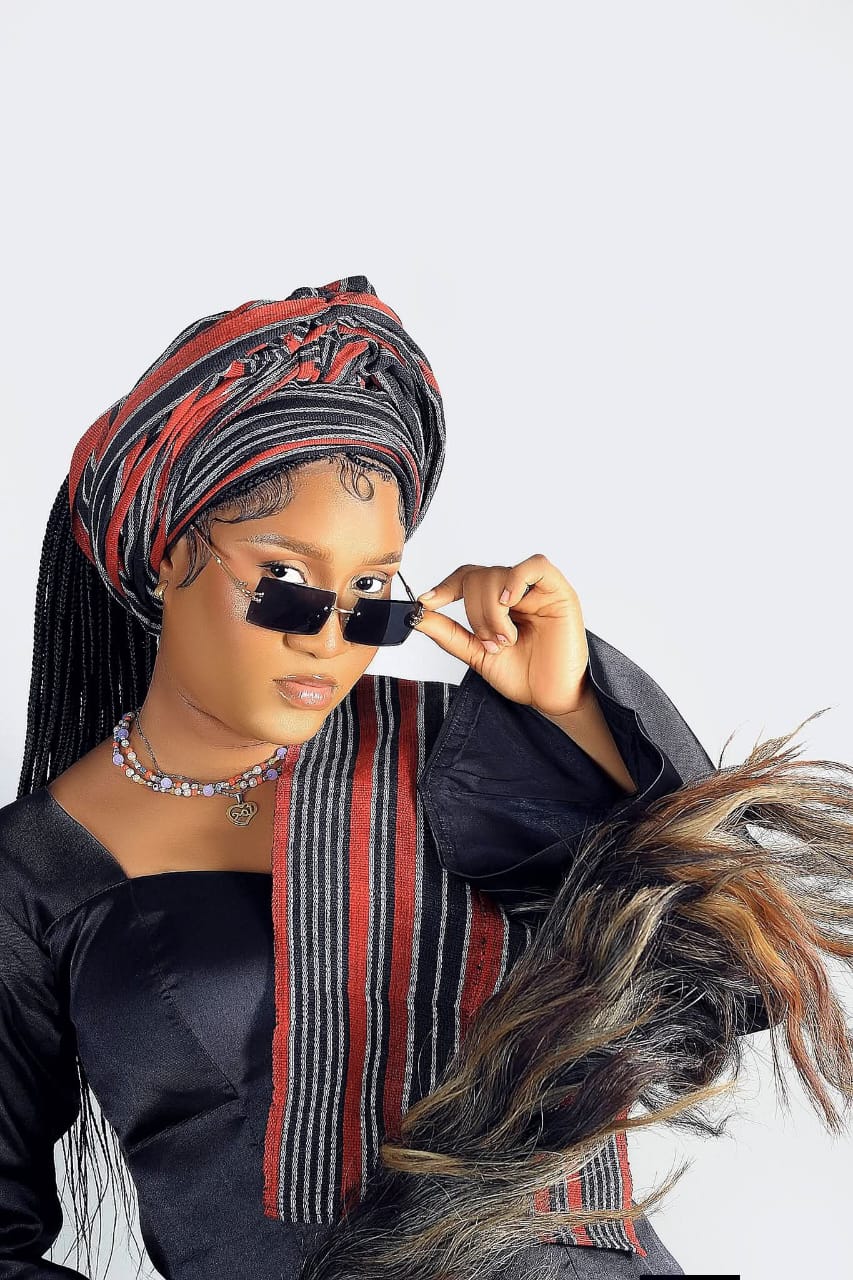 Woman in a red and black striped headwrap and rimless sunglasses draped in a fur stole