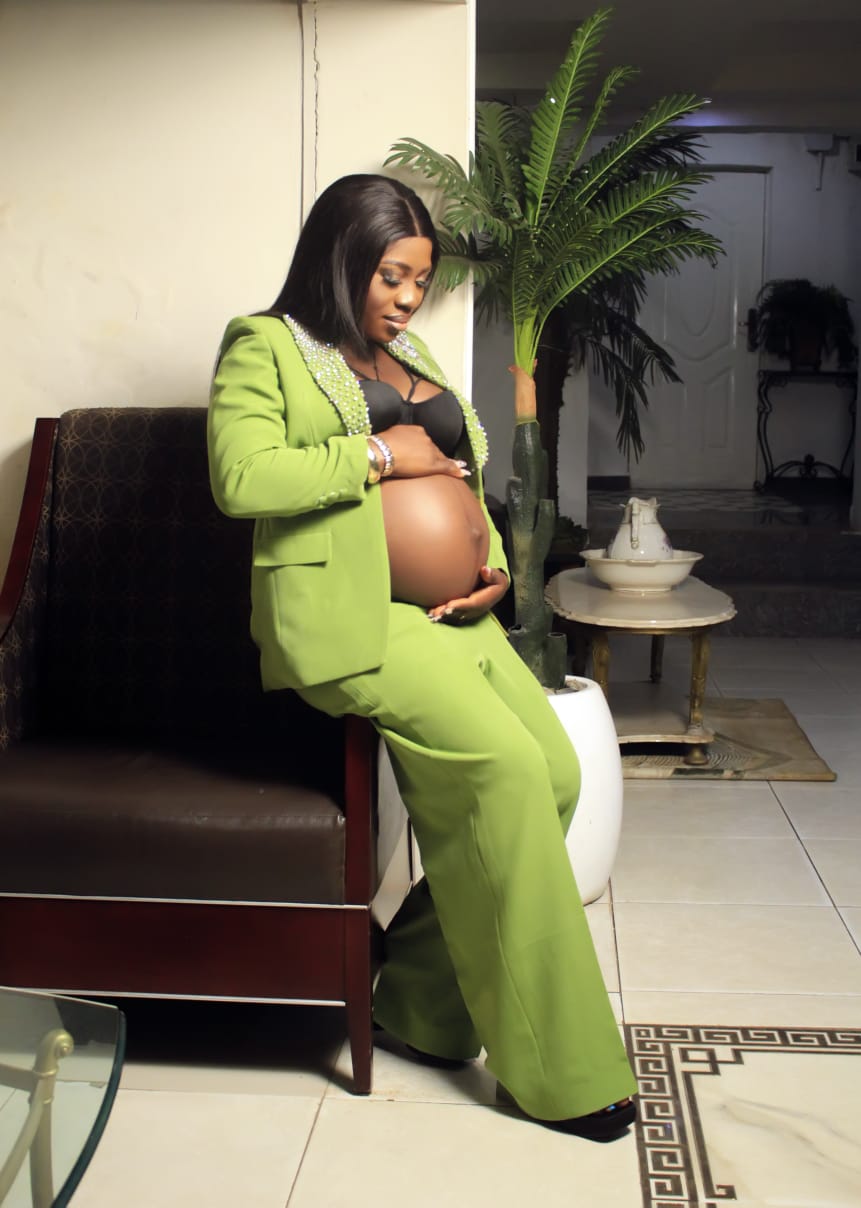 Pregnant woman in a green pearl-trimmed suit posing indoors